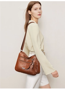 Detail view of brown soft leather crossbody bag with multi-zipper layers and flap pocket