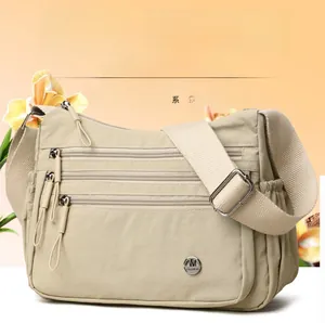 Close-up of beige nylon crossbody bag featuring three parallel zippered compartments