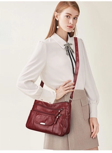 Detail view of deep red multi-layered leather crossbody bag worn by a model in soft lighting