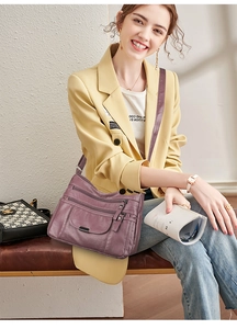 Detail of a purple multi-zipper leather crossbody bag worn with a yellow blazer jacket