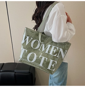 Fashionable large green tote bag with white lettering shown in a lifestyle street setting