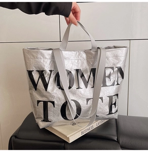 Detail of silver metallic tote bag featuring pleated texture and WOMEN TOTE bold logo