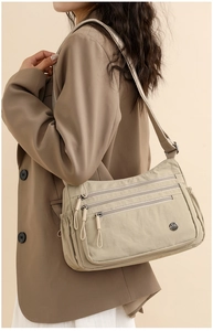 Detail of light beige nylon crossbody bag featuring three-layer zipper pockets and adjustable strap