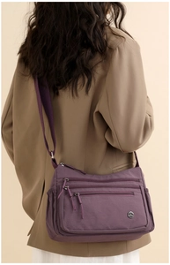 Detail of purple nylon crossbody bag with multiple zip pockets and metal logo on a model
