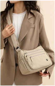 Detail of beige nylon crossbody bag featuring multiple pockets and a wide woven strap