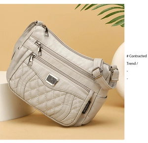 Detail view of the quilted texture and multi-layer zippers on a light grey crossbody bag