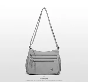 Gray nylon crossbody bag featuring multiple front zipper pockets and adjustable strap