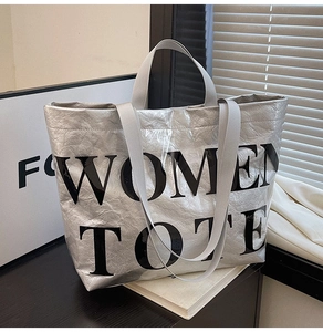 Detail of silver metallic tote bag featuring bold black WOMEN TOTE text and textured fabric