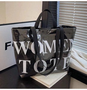 Detailed view of large black glossy tote bag with white WOMEN TOTE print on dark wooden surface