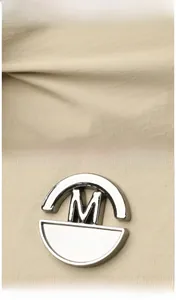 Macro shot of beige fabric texture and round silver metal logo featuring an M engraving