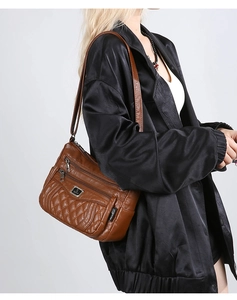 Detail view of brown quilted shoulder bag with multiple zippers and silver logo detail