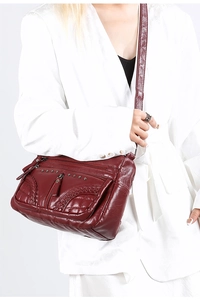 Detail of burgundy leather crossbody bag with tassels and decorative studs on white suit
