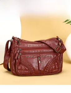 Detail of burgundy soft leather crossbody bag with multiple zippers and woven rivet texture