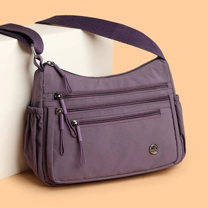 Purple nylon crossbody bag with multi-zipper compartments and wide woven shoulder strap