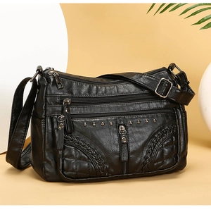 Detail of black multi-pocket crossbody bag with woven trim and silver rivet accents