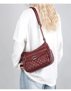 Detail of quilted maroon crossbody bag with adjustable strap and multiple zipper pockets