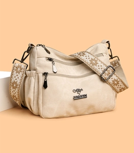 Detail of cream fabric crossbody bag featuring multiple zippers and jacquard shoulder strap