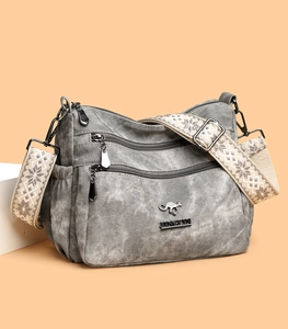 Detail of gray canvas crossbody bag featuring three-layer zippers and wide strap