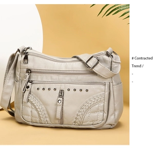 Detail of soft beige leather crossbody bag featuring multiple zippers and metal rivets