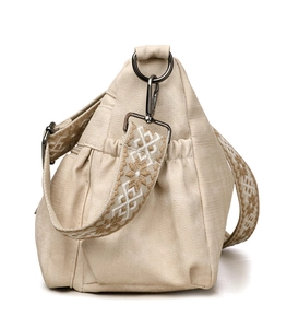 Detail view of beige canvas tote bag with bohemian embroidered strap and metal hardware