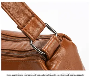Detail of silver D-ring buckle and smooth dual zippers on brown pebbled leather bag