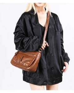 Detailed view of brown faux leather crossbody bag with multiple zippers and woven edges