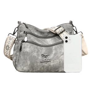 Grey multi-zipper canvas shoulder bag with wide geometric strap and phone for scale
