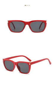 Detail of red square sunglasses featuring grey lenses and gold metal corner accents