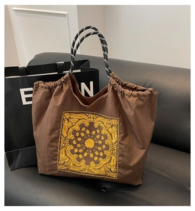 Detail of a brown tote bag with yellow paisley embroidery and woven rope handle
