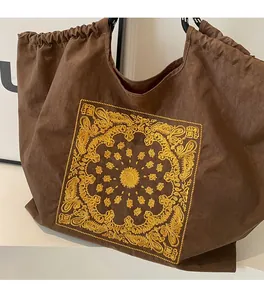 Detail of dark brown tote bag featuring yellow embroidery and drawstring closure