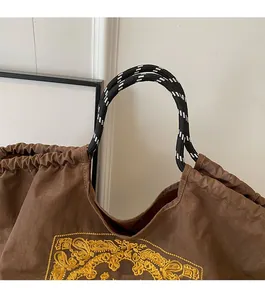 Detail of a brown canvas tote bag with yellow ethnic embroidery and woven handles