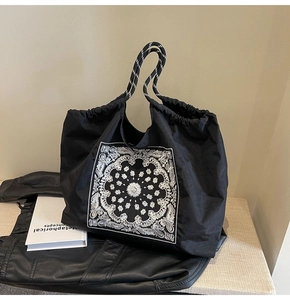 Close-up of black paisley drawstring tote bag with striped rope handles on a beige surface