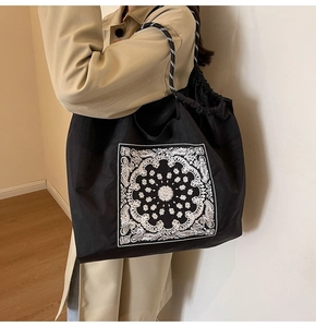 Detail of black tote bag with white paisley pattern and striped rope handles on shoulder