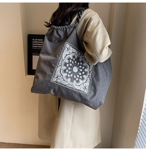 Detailed view of grey tote bag with paisley print and braided rope handles on model