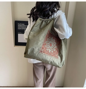 Detail of army green canvas drawstring bag with paisley embroidery and woven strap