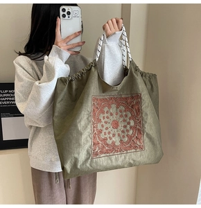 Macro detail of green canvas tote bag featuring brown floral embroidery and white rope handles