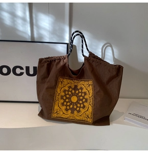 Detail of dark brown canvas tote bag featuring yellow bandana print and braided rope handles
