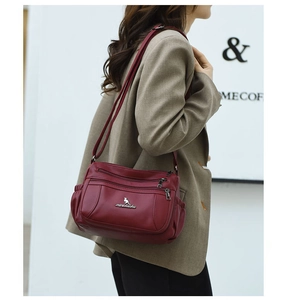 Detail view of burgundy leather crossbody bag with multiple zippers and side pockets