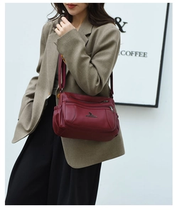 Deep burgundy shoulder bag with multiple zippers and metallic logo worn by a model