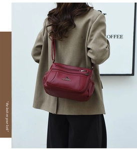 Detail of burgundy multi-zippered shoulder bag with kangaroo logo on model