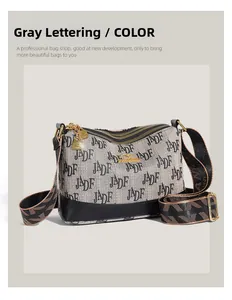 Detail of grey crossbody bag featuring letter patterns and gold-tone zipper accents