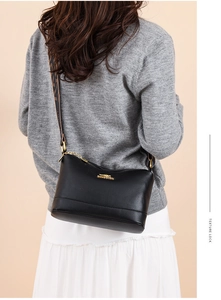 Detail of black pebbled leather handbag with gold zipper and patterned woven strap