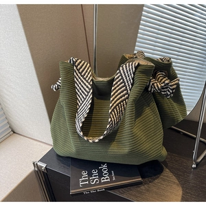 Detail of dark green corduroy tote bag with geometric woven straps on a shelf