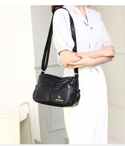 Detail of a black multi-zip crossbody bag with soft leather texture and silver logo