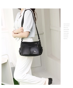 Model showcasing a black faux leather crossbody bag with multiple zipper pockets and logo