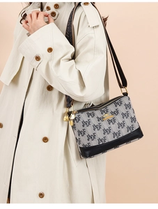 Gray canvas crossbody bag with letter print and gold kangaroo logo on beige trench coat