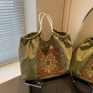 Olive green paisley embroidered drawstring tote bag with woven rope handles in soft natural light