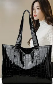 Detail of large black tote bag with glossy crocodile embossed texture and slim straps