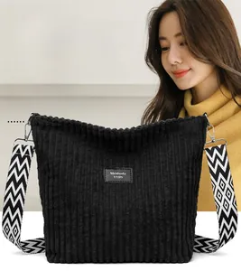 Detail of black corduroy tote with textured zigzag strap and leather brand label