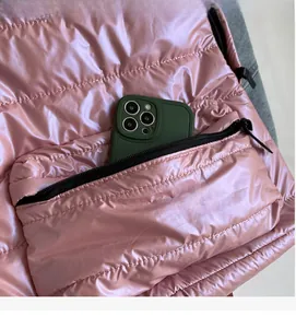 Detailed close-up of the pink quilted backpack showing a zippered pocket with a phone inside